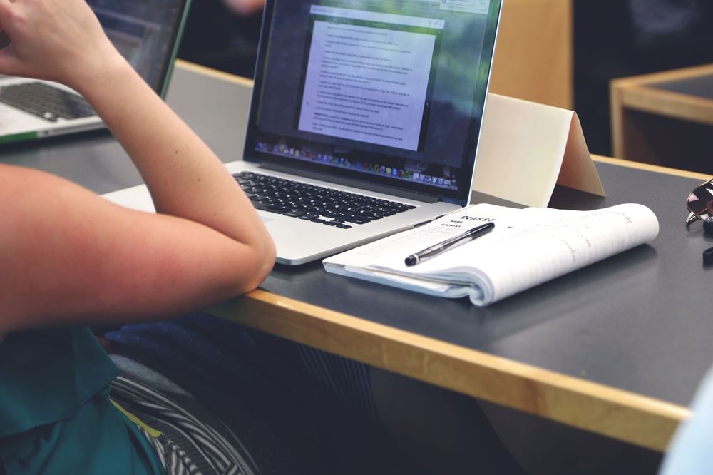 Uno studente universitario concentrato mentre usa un moderno notebook per studiare, circondato da libri e appunti, su un campus.