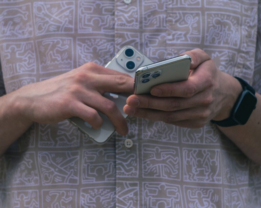 Un uomo valuta due smartphone, uno più vecchio top di gamma e uno nuovo medio gamma, in un gesto di scelta e comparazione.