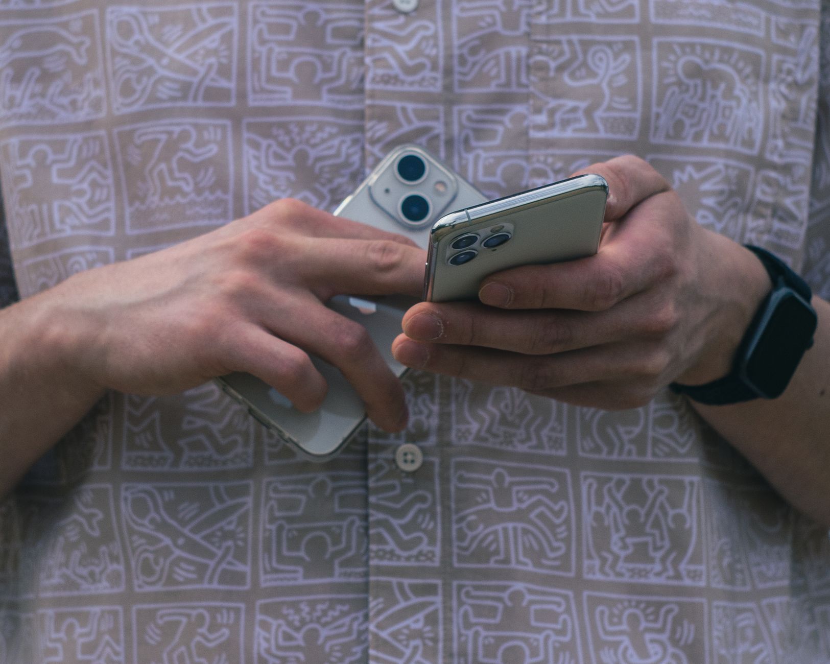 Un uomo valuta due smartphone, uno più vecchio top di gamma e uno nuovo medio gamma, in un gesto di scelta e comparazione.